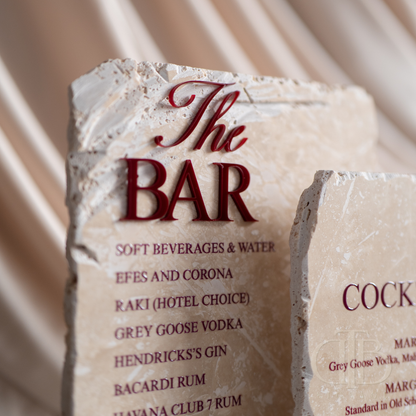 Stone menu board with 'The Bar' and drink options on a draped fabric background