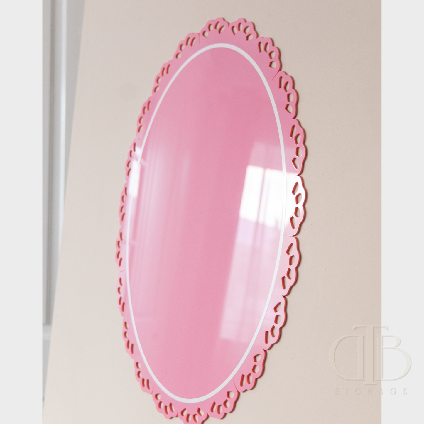 Pink decorative acrylic signage with scalloped edge on a light beige wall
