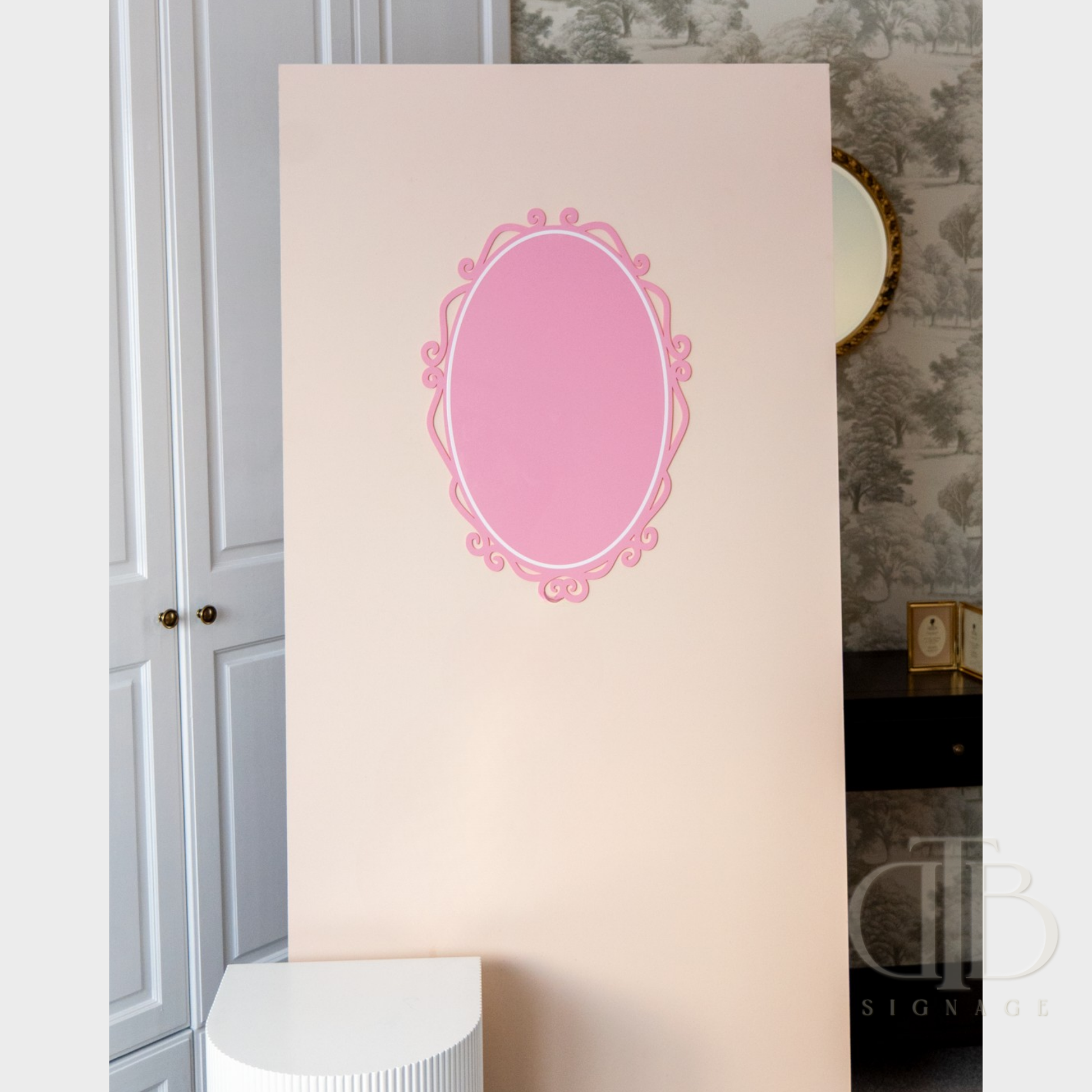 Decorative pink oval frame on a beige background with a gray wall and white door in the background.