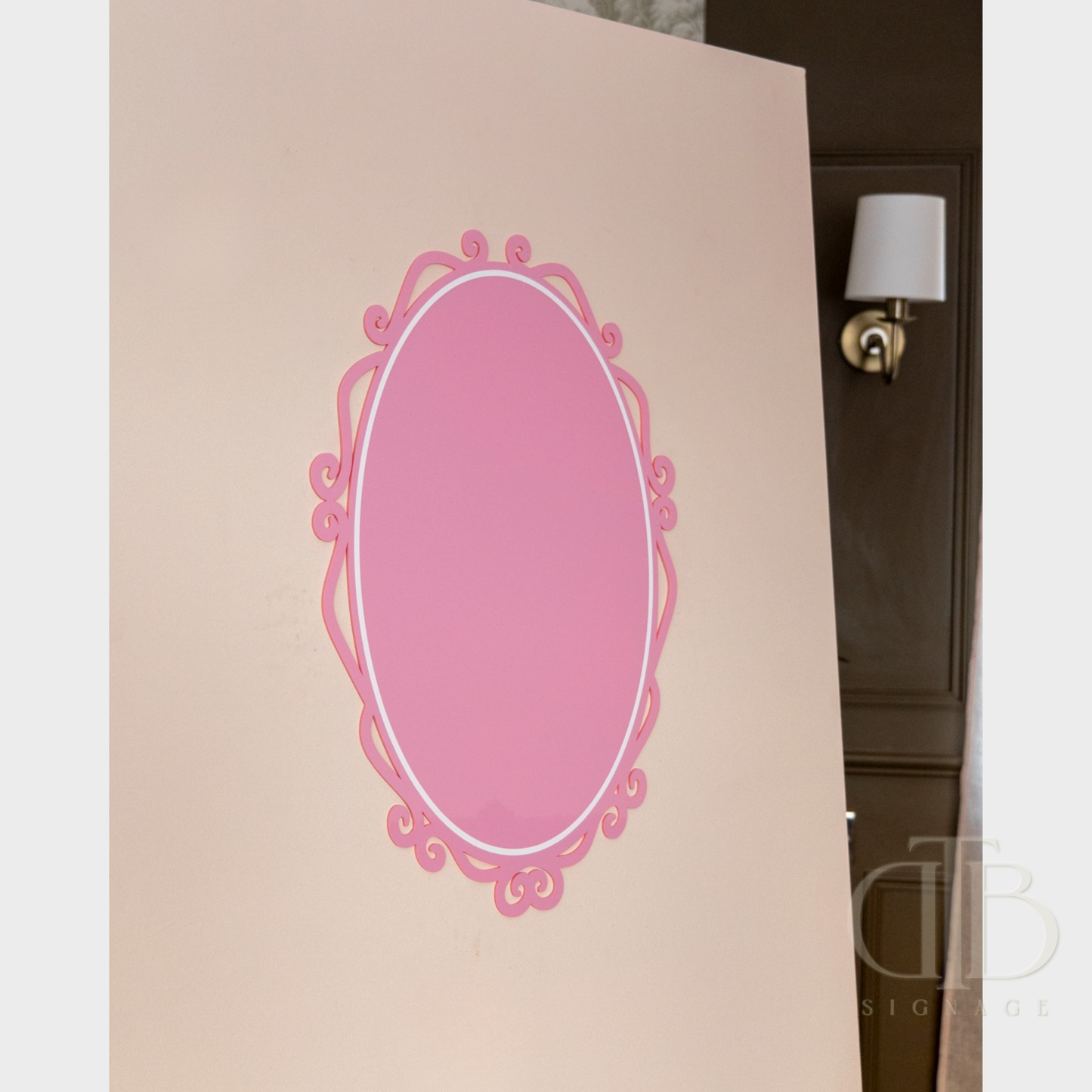 Decorative pink oval acrylic signage on a beige wall with a lamp in the background.
