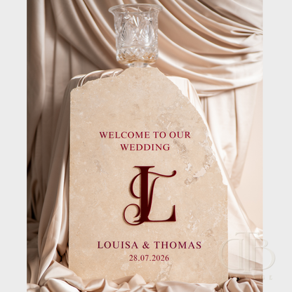Wedding welcome sign with 'Welcome to our wedding' text and monogram, placed on a draped fabric background.
