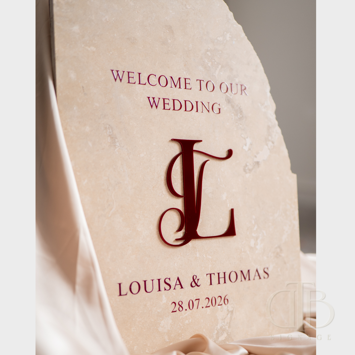 Personalized wedding welcome sign with monogram 'L' and names Louisa & Thomas on a stone surface.