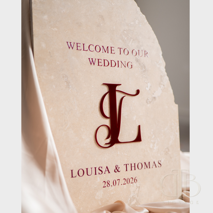 Personalized wedding welcome sign with monogram 'L' and names Louisa & Thomas on a stone surface.