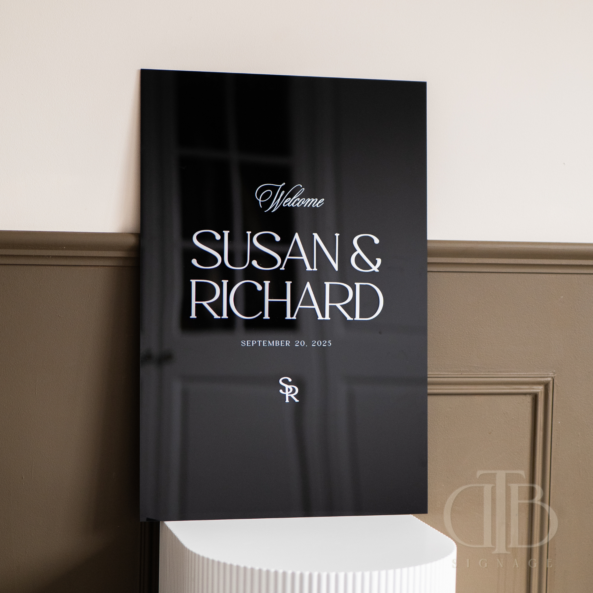 Black book with 'Welcome SUSAN & RICHARD' text on a beige wall