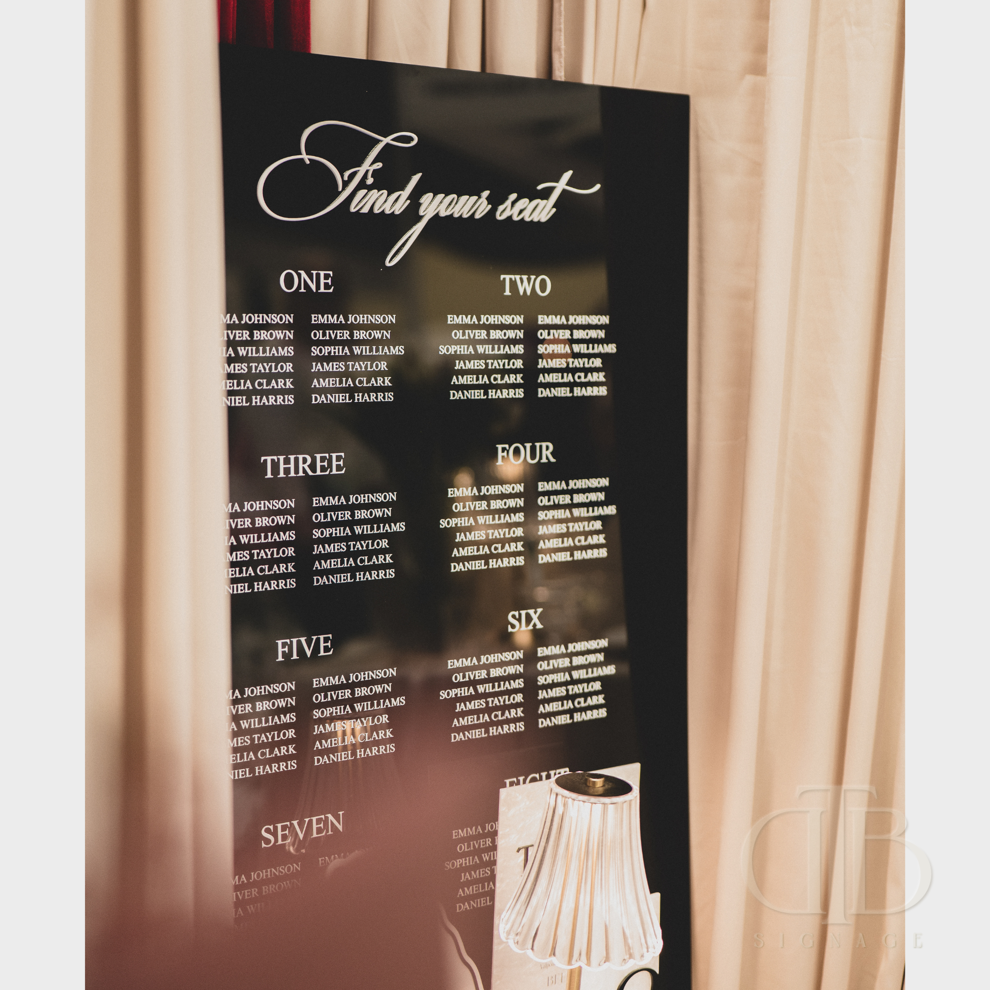 Seating chart for an event with names listed on a black board against a curtain background