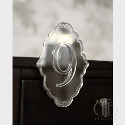 Silver mirror number '9' on a decorative ornate plaque stuck on a table.