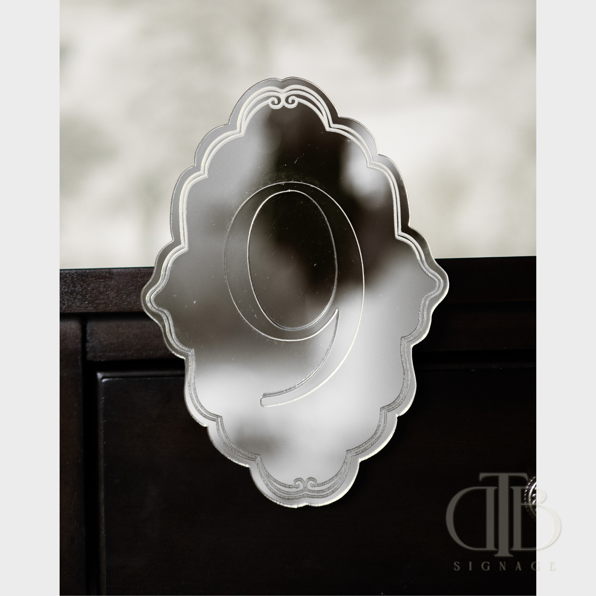 Silver mirror number '9' on a decorative ornate plaque stuck on a table.